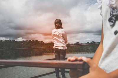 Rear view of women standing by railing against cloudy sky