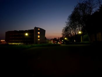 Illuminated street by buildings against sky at night