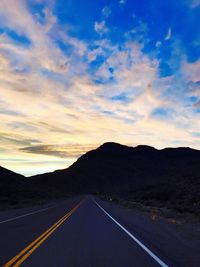 Road amidst silhouette landscape against sky during sunset