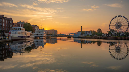 Scenic view of river by buildings against sky during sunset