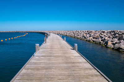 Pier over sea against clear blue sky