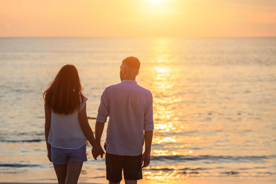 Rear view of couple standing on beach during sunset