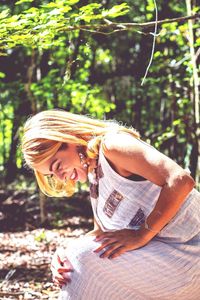 Side view of smiling woman crouching against trees in forest