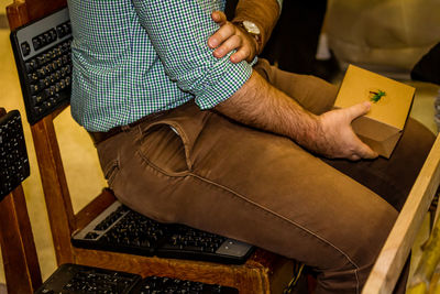 Midsection of man holding box while sitting on computer keyboards at chair