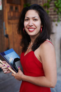 Portrait of smiling young woman with book standing outside language school