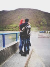 Young couple embracing while standing by railing on road
