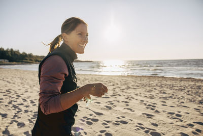 Side view of happy mature woman at beach on sunny day