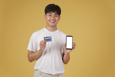 Portrait of smiling man holding camera while standing against yellow background