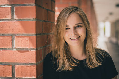 Portrait of smiling beautiful woman with blond hair standing by architectural column