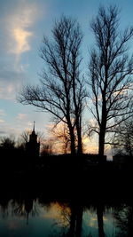 Silhouette of bare trees by river at sunset