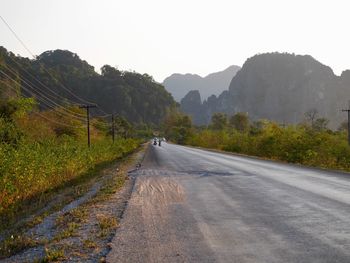 Country road by mountains against sky