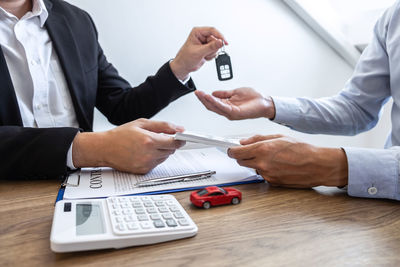 Agent giving car key to customer by papers and currency on table