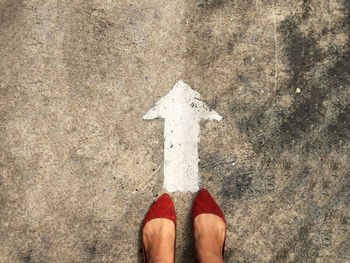 Low section of woman standing in front of arrow sign on road