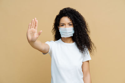 Portrait of woman wearing mask standing against beige background