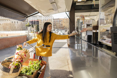 Happy young woman standing with cargo bike and buying dessert from shop