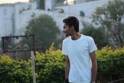 Young man looking away while standing against plants