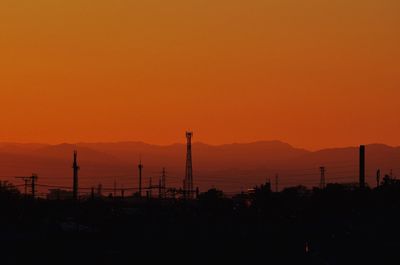 Silhouette mountains by sea against orange sky