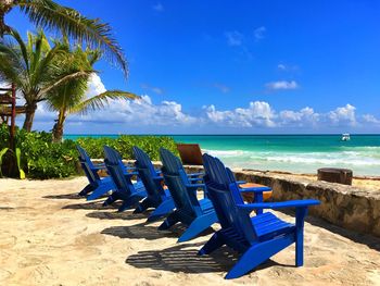 Blue empty chairs at beach against sky during summer