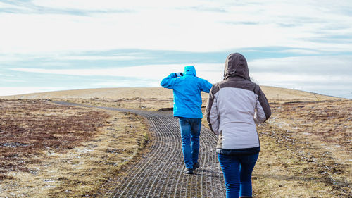 Rear view of man and woman walking on land against sky