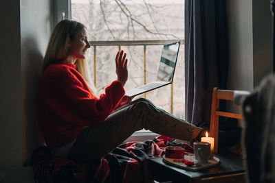 Side view of woman sitting by window at home
