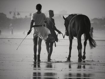 Men riding horse on sea shore against sky