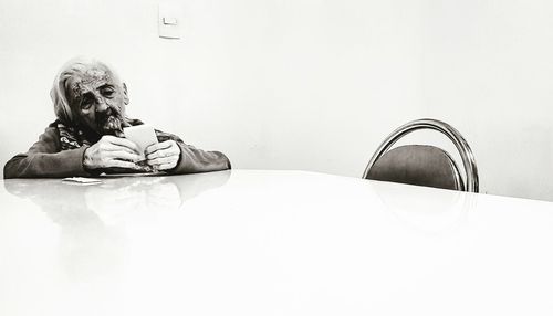 Portrait of man sitting on table against wall at home