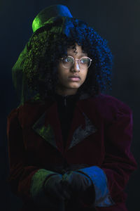 Portrait of young woman standing against black background