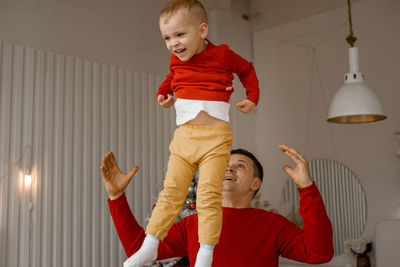 Cheerful happy father throwing up his adorable laughing son in bright room with christmas interior