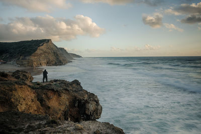 Man standing on rock formation against sea during sunset