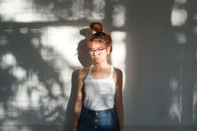 Young woman looking away while standing against wall