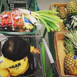 High angle view of child sitting on shopping cart with fruits and vegetable in it