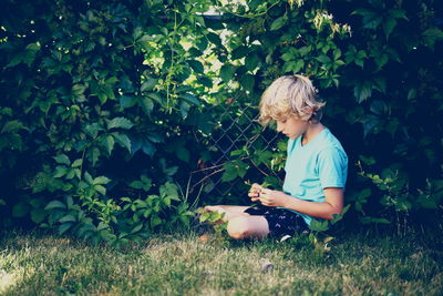 Boy sitting on grass against trees