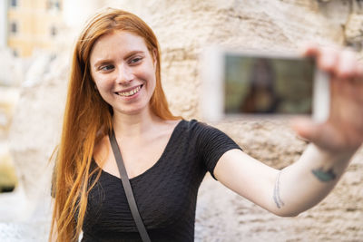 Cheerful redhead woman taking selfie in city