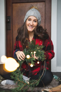 Portrait of smiling woman holding wreath while sitting at home during christmas