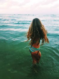 Rear view of young woman in bikini standing at sea against sky