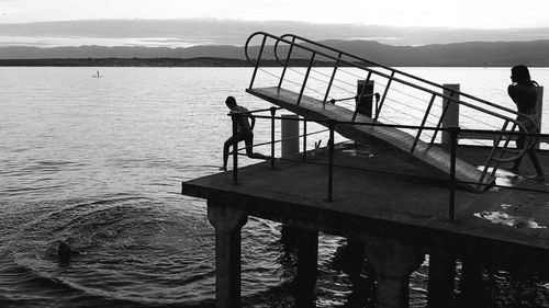 Silhouette people standing on pier by lake against sky