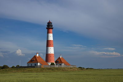 Lighthouse on field by building against sky