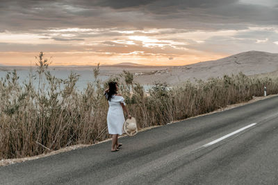 Rear view of young woman in white dress standing on road. summer, wanderlust, travel.