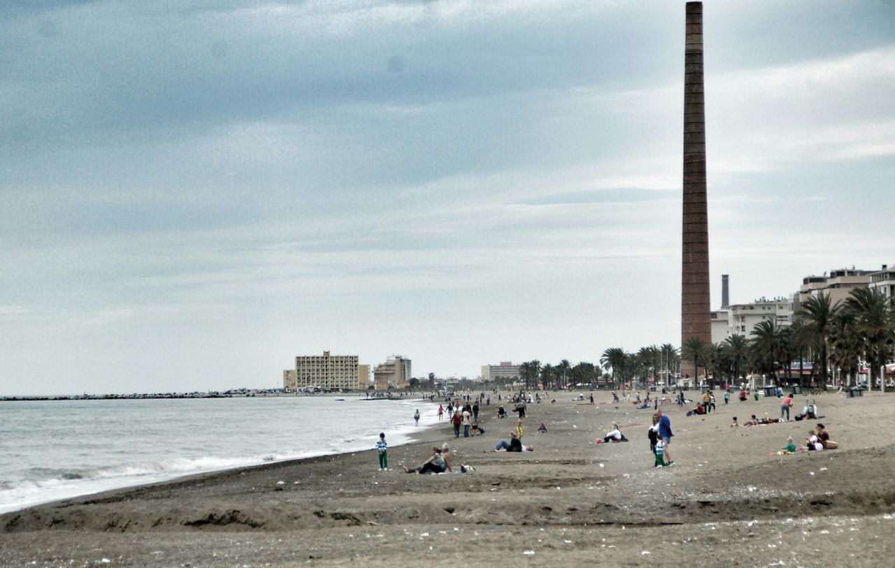 beach, large group of people, water, sky, architecture, sea, built structure, shore, lifestyles, building exterior, leisure activity, men, city, person, mixed age range, vacations, tourist, sand, cloud - sky