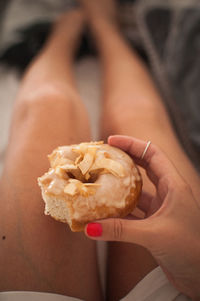 Midsection of woman holding fresh donut on bed at home