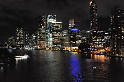 Illuminated buildings by river against sky at night