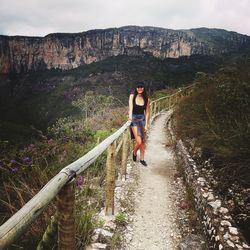 Portrait of smiling young woman standing on footpath against mountain