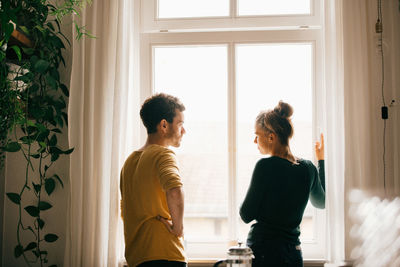 Couple talking while standing by window at home