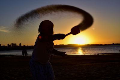 Silhouette woman on beach against sky during sunset