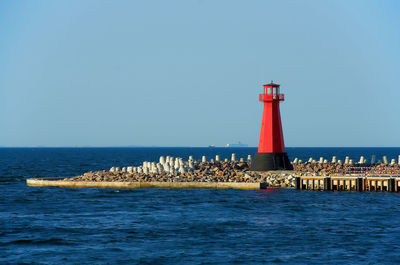 Lighthouse by sea against clear sky