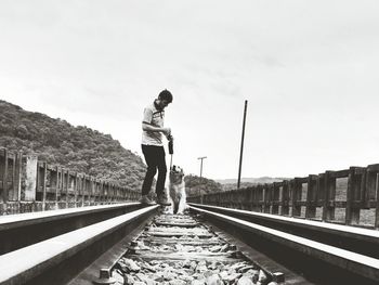 Full length of man with golden retriever standing on railway bridge against cloudy sky