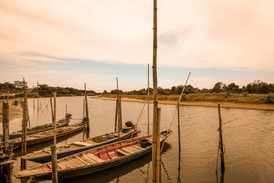 Sailboats moored in river against sky during sunset