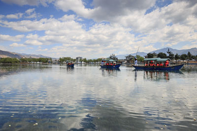 Boats in sea against cloudy sky