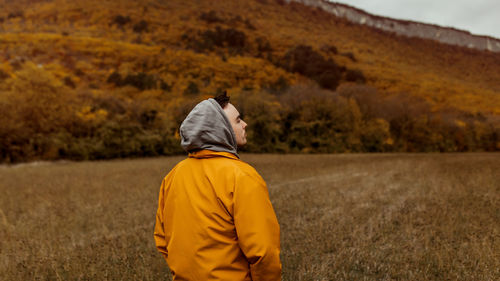 Young male millennial in a yellow jacket on a trip in the mountains in autumn forest