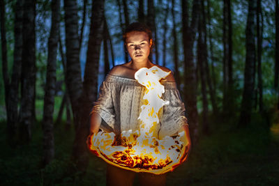 Digital composite image of woman holding fire while standing in forest